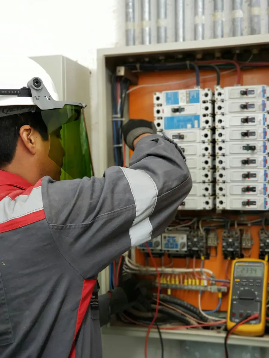 Technician in arc-rated face shield testing an energised panel